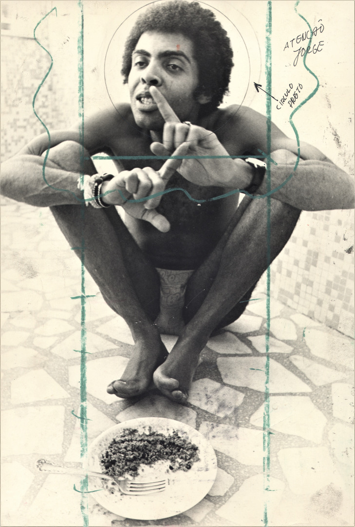 Gilberto Gil sem camisa, agachado com o dedo nos lábios, diante de um prato; cópia de arquivo com marcações de diagramação